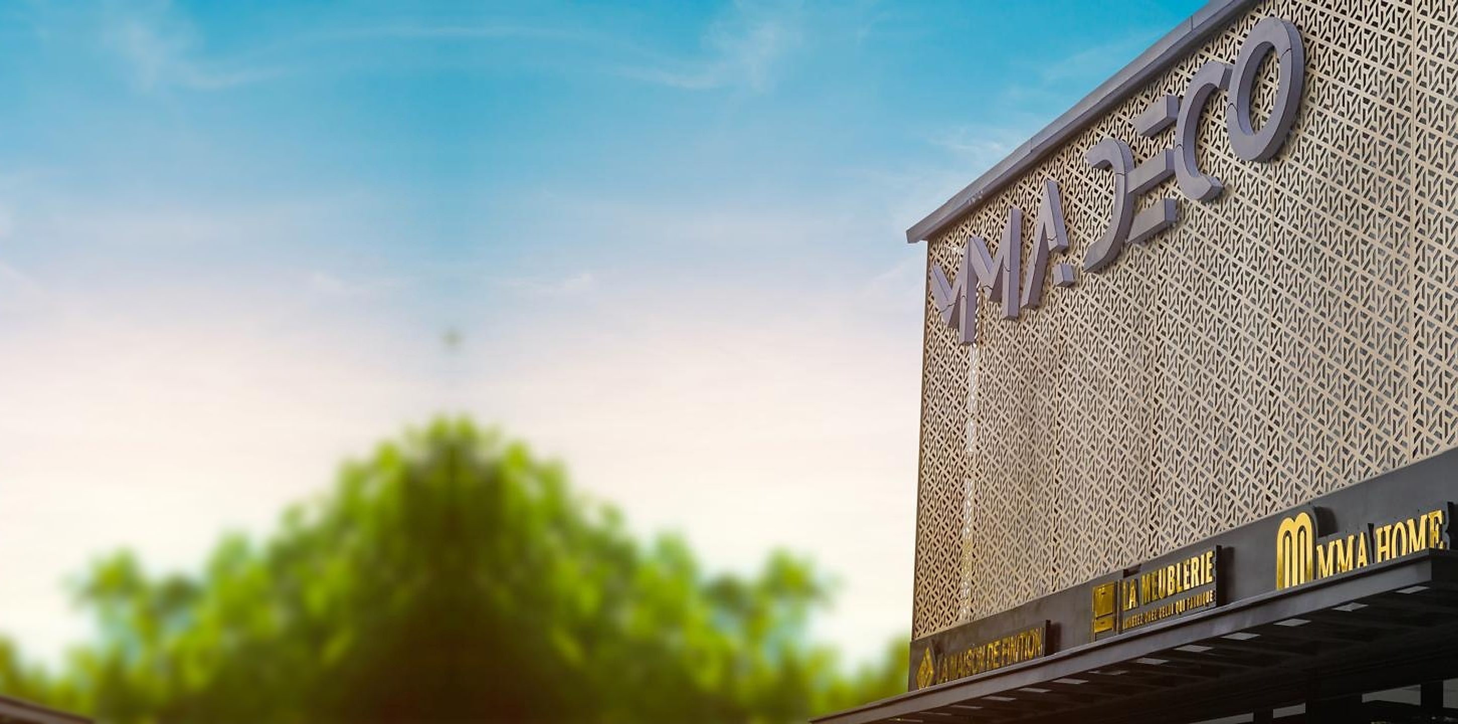Façade du magasin MMA DÉCO : l'enseigne sur un mur ajouré, et les enseignes dorées La Maison de Finition, La Meublerie et MMA Home